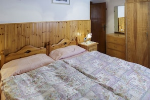 Una camera da letto con una testiera in legno, due letti, un comodino con una lampada, una cassettiera e uno specchio.