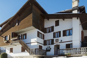 Un edificio su due piani con facciata in legno, diverse finestre e un balcone con ringhiera.