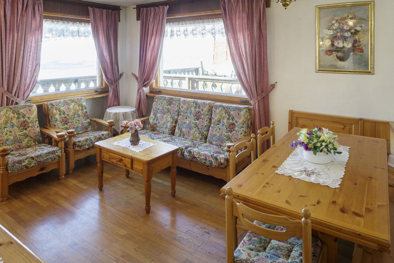 Una habitación acogedora con una mesa de comedor de madera, sofás con estampado floral y una pequeña mesa redonda con un jarrón de flores.