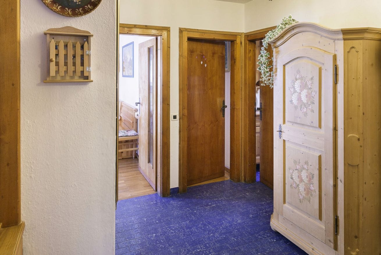 A hallway with wooden doors, a blue carpet, and a wooden cabinet with a floral design.