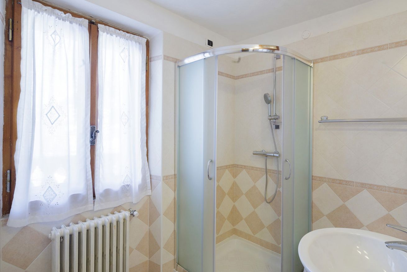 A bathroom with a glass shower enclosure, a white sink, and patterned wall tiles.