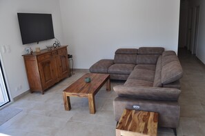 A living room with a wooden coffee table, a brown leather sofa, a wooden cabinet, and a television mounted on the wall. - Charming vacation rental: pool, stunning view, dogs welcome, enclosed garden, near Nyons. (Curnier)