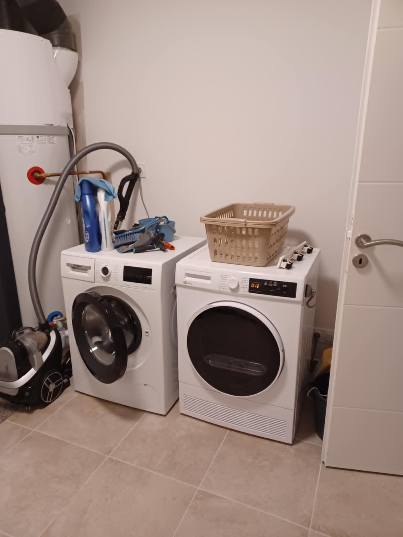 Un espace buanderie comprenant deux machines à laver, un panier et des produits de nettoyage.
