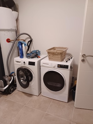A laundry area with two washing machines, a basket, and cleaning supplies. - Charming vacation rental: pool, stunning view, dogs welcome, enclosed garden, near Nyons. (Curnier)