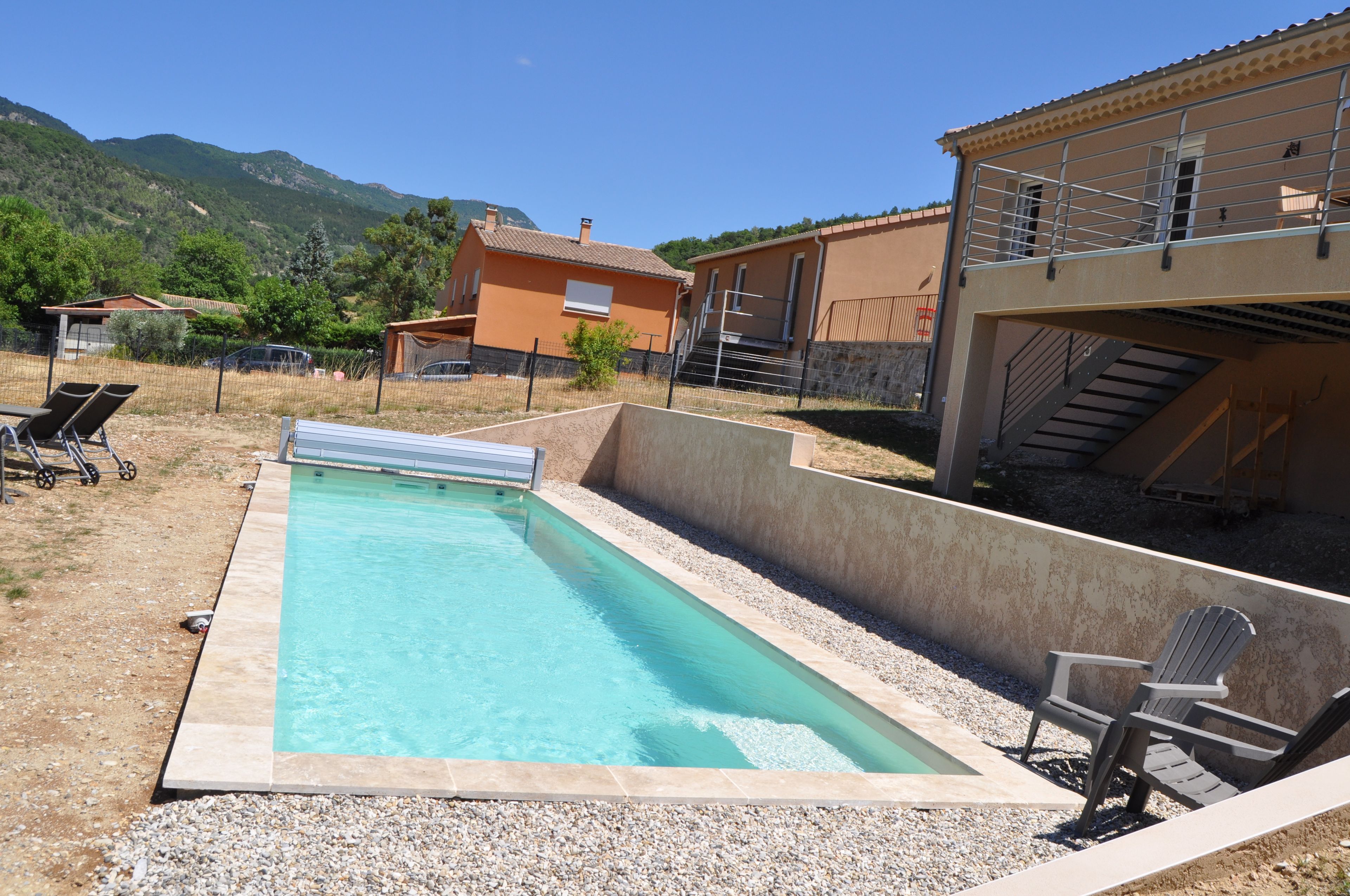 A rectangular swimming pool with a pebble-lined edge, surrounded by a gravel area with lounge chairs.