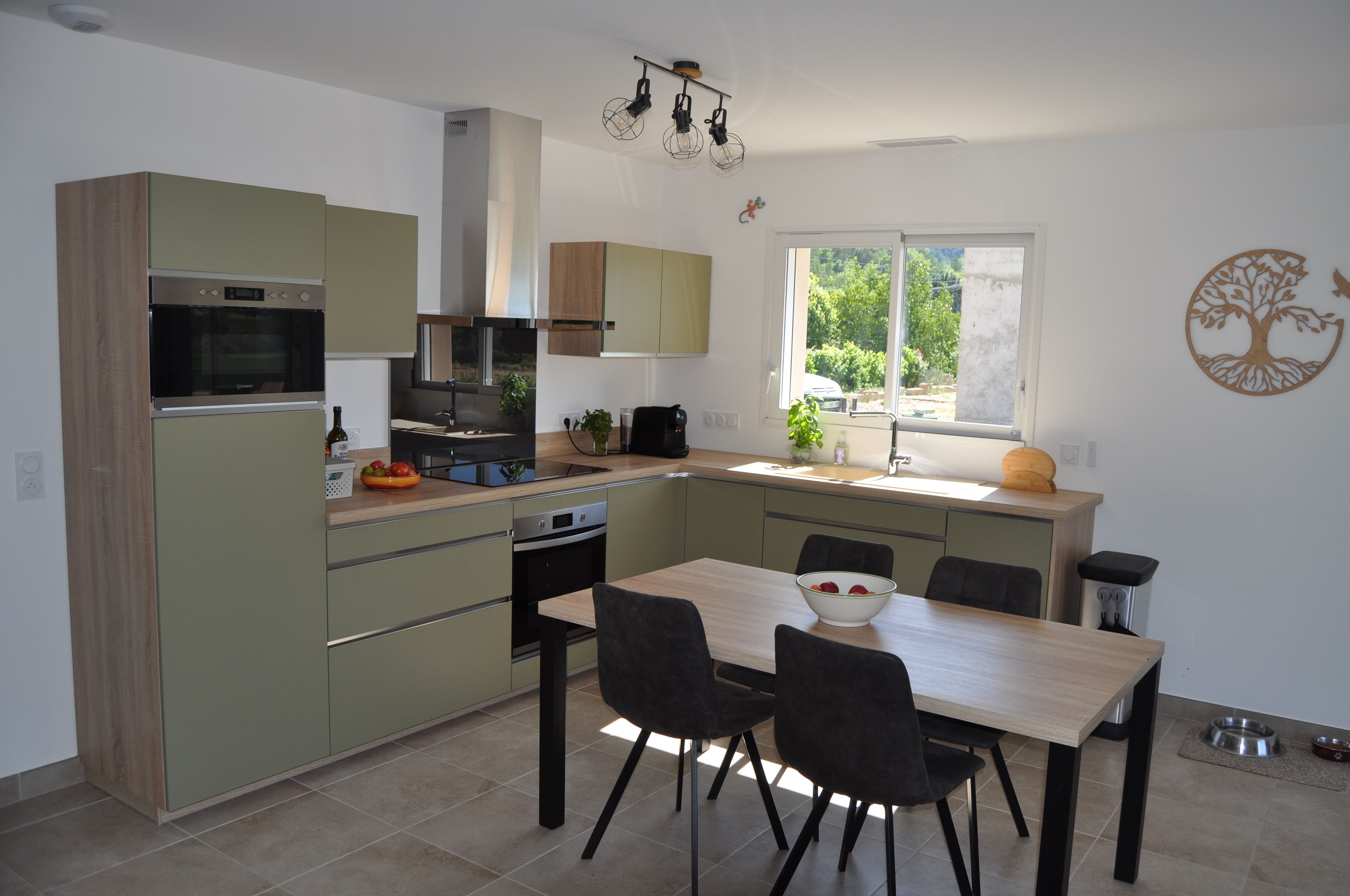 A modern kitchen with a dining area, featuring a built-in oven, a stove, a sink, and a window with a view of greenery.