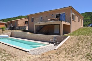 A two-story house with a swimming pool, a covered patio, and a view of a forested hill. - Charming vacation rental: pool, stunning view, dogs welcome, enclosed garden, near Nyons. (Curnier)