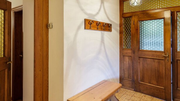Un banco de madera en un pasillo con una puerta y una lámpara de pared.
