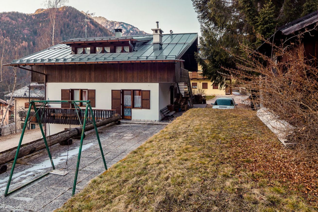 A two-story wooden house with a metal roof, a swing set, and a car parked in the driveway.