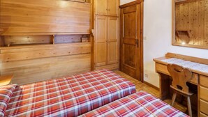 Una habitación con dos camas, un armario de madera y un escritorio con una silla.