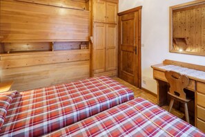 Een kamer met twee bedden, een houten garderobe en een bureau met stoel.