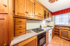 Una cocina con armarios de madera, estufa a gas, lavavajillas y una ventana con cortina roja.