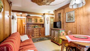 Een gezellige kamer met een bank, een houten kast en een eettafel met stoelen.