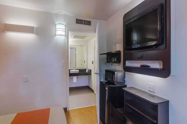 A hotel room with a TV, a microwave, and a small kitchenette area.
