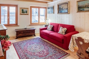 Una stanza con un divano rosso, mobili in legno, un tappeto decorato e quadri appesi al muro.
