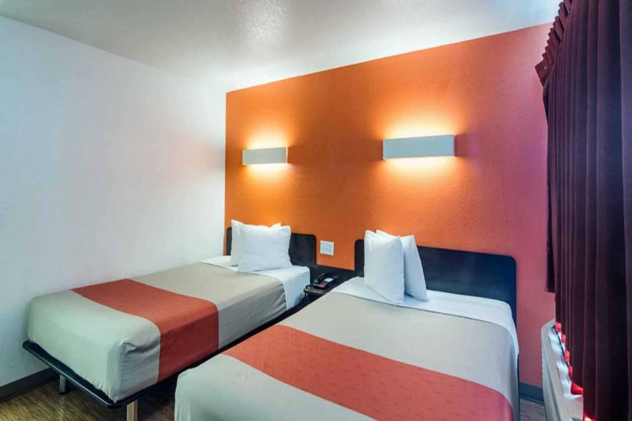 A hotel room with two single beds, a nightstand, and a wall-mounted light fixture.