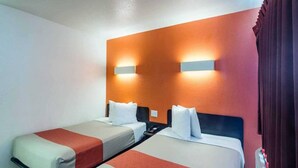 Habitació d'hotel amb dos llits individuals, una tauleta de nit i un llum penjada a la paret.
