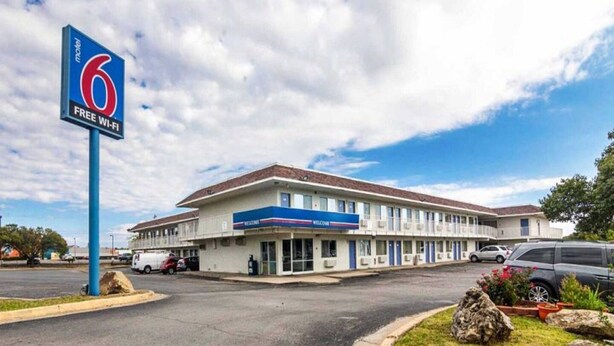 Un motel amb un gran rètol, un aparcament i un edifici amb terrat pla.