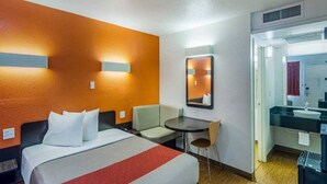 Habitació d'hotel amb llit, escriptori, cadira, taula petita, mirall i bany amb rentapla i vàter.