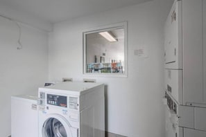 A laundry room with stacked washers and dryers, a large mirror on the wall, and a door leading to another room.