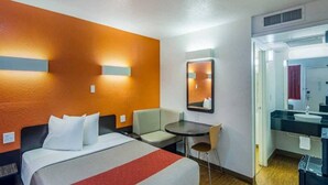 Habitació d'hotel amb llit, escriptori, cadira, taula petita, mirall i bany.