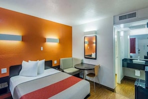 Ein Hotelzimmer mit Bett, Schreibtisch, Stuhl, einem kleinen Tisch, einem Spiegel und einem Badezimmer.