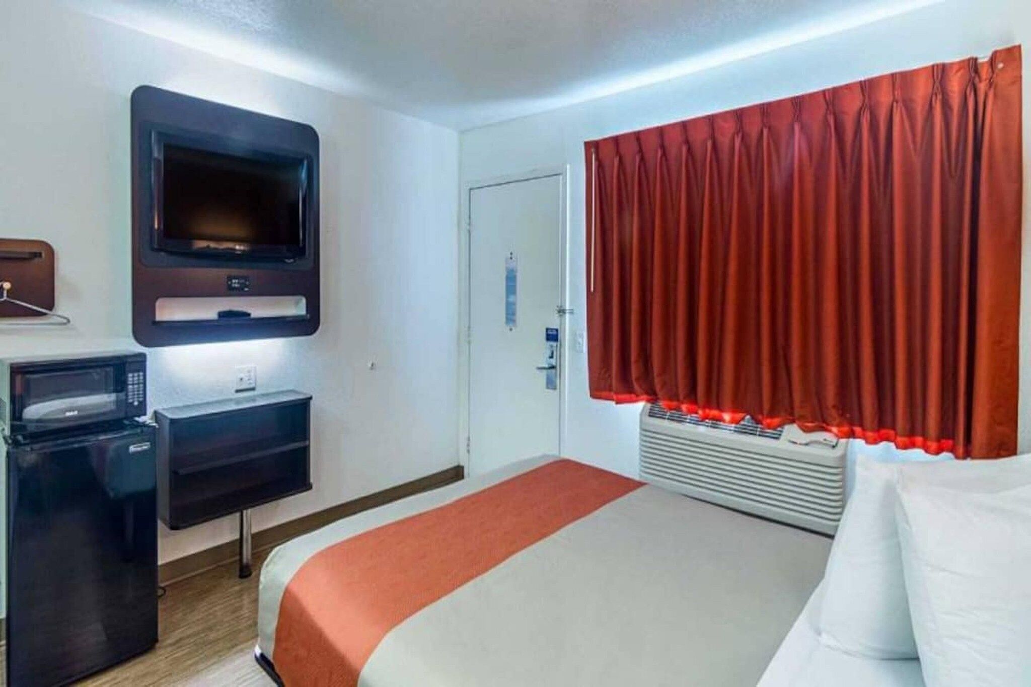 Una habitación de hotel con una cama, un escritorio con computadora, un televisor y una cortina roja.