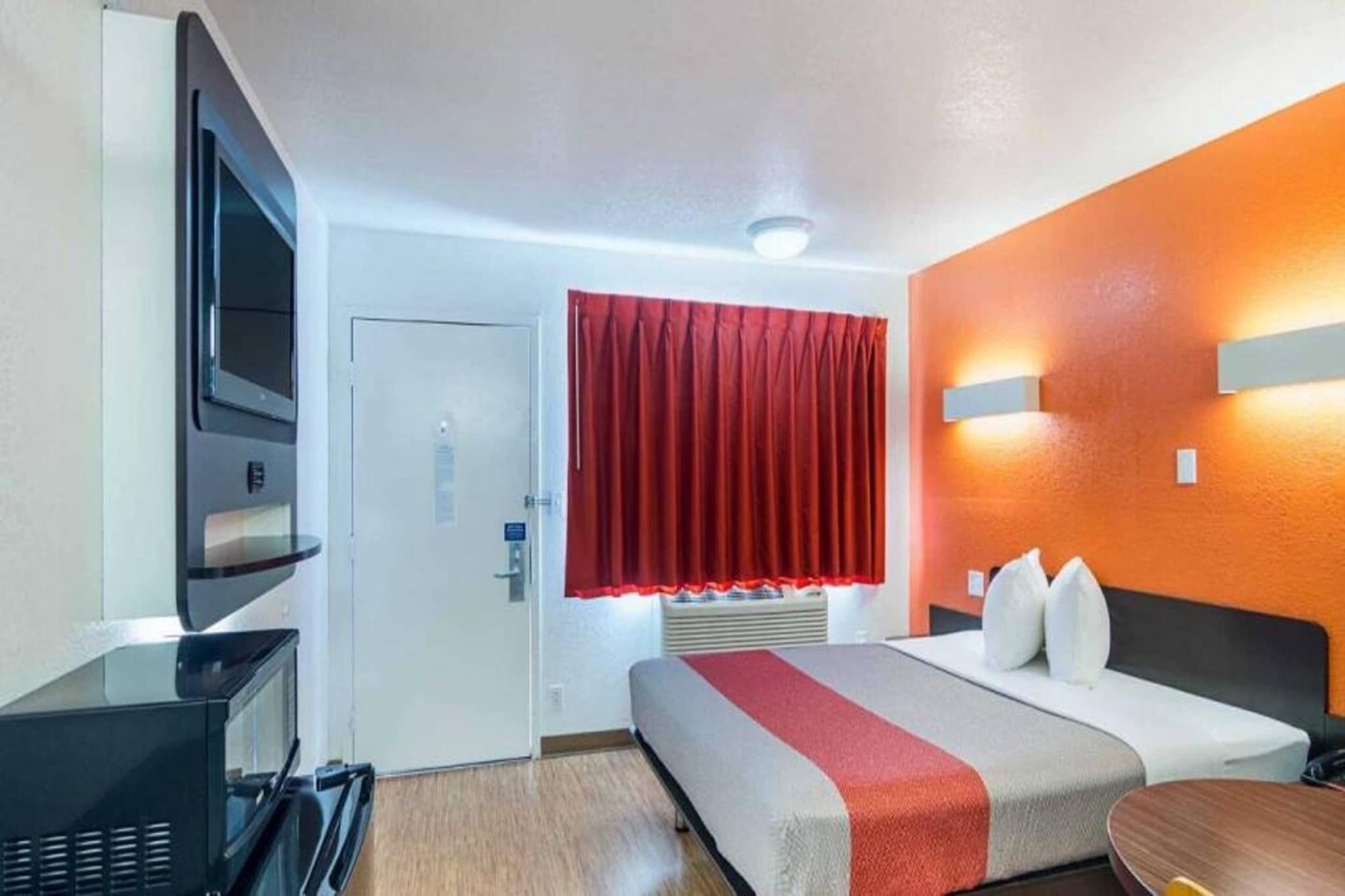 A hotel room with a bed, a desk, a television, and a red curtain.