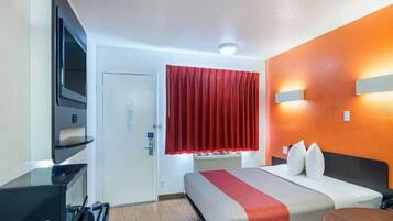 A hotel room with a bed, a desk, a television, and a red curtain.