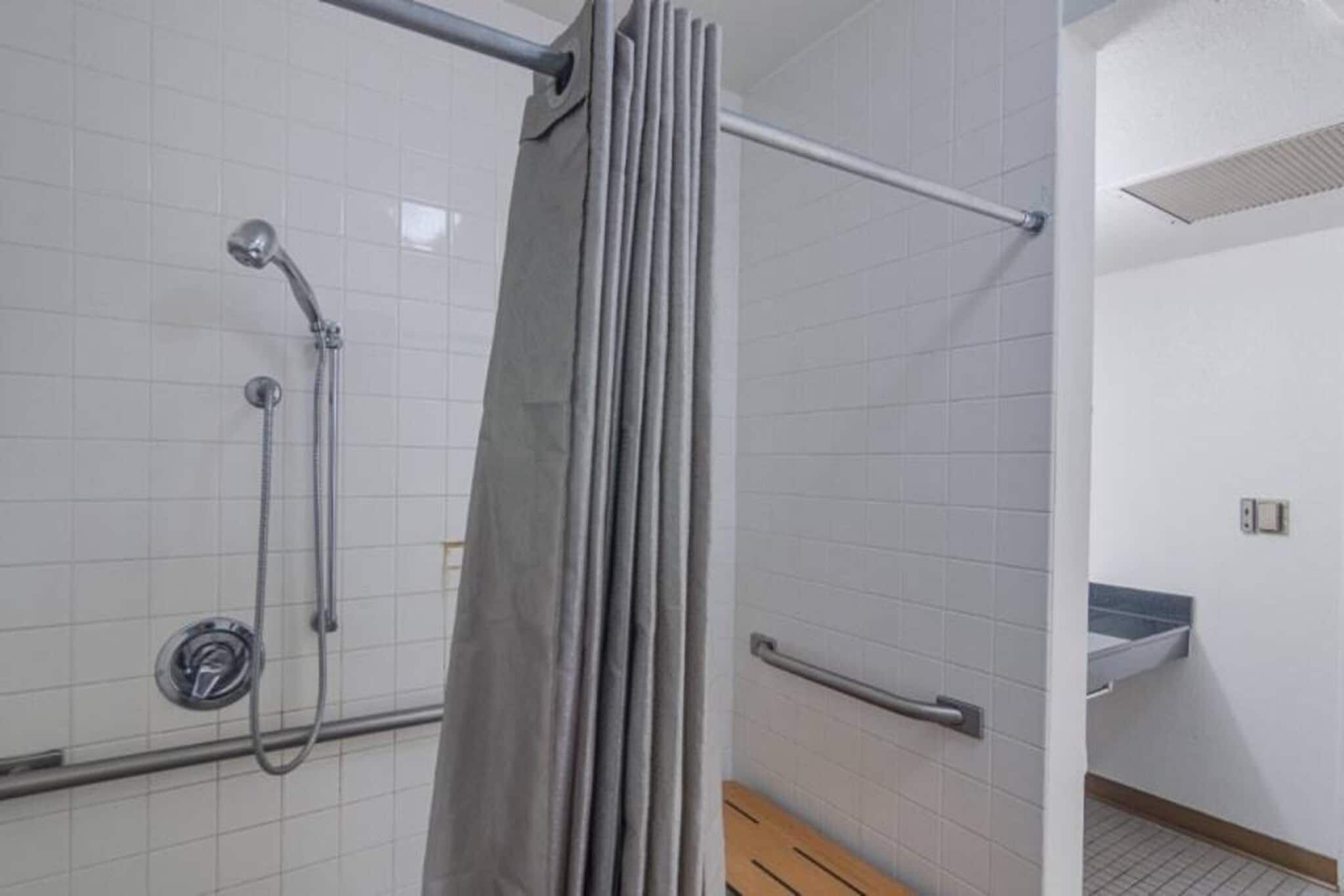 A shower area with a handrail, a showerhead, and a curtain.