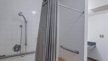 A shower area with a handrail, a showerhead, and a curtain.