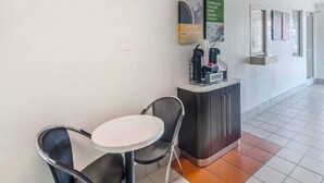 Rebuda d'hotel amb taulell de recepció, zona de cafè i zona d'estar amb cadires i taula.
