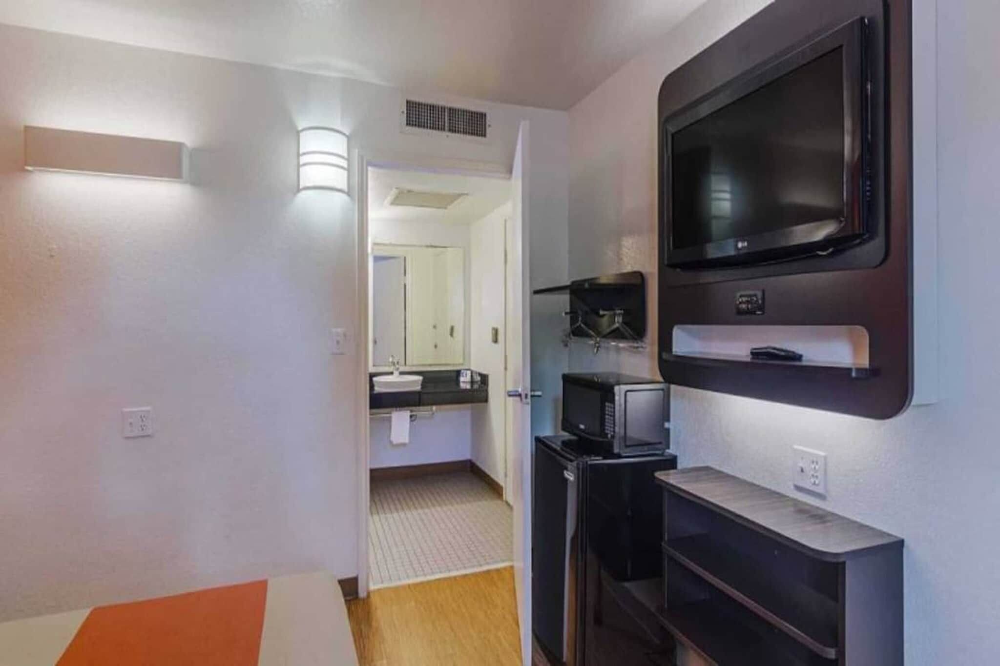 A hallway with a TV mounted on the wall, a microwave, and a small refrigerator.