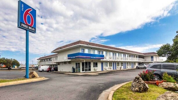 Motel amb un cartell gran que indica Wi-Fi gratuït, un aparcament i un edifici amb teulada plana i diverses finestres.