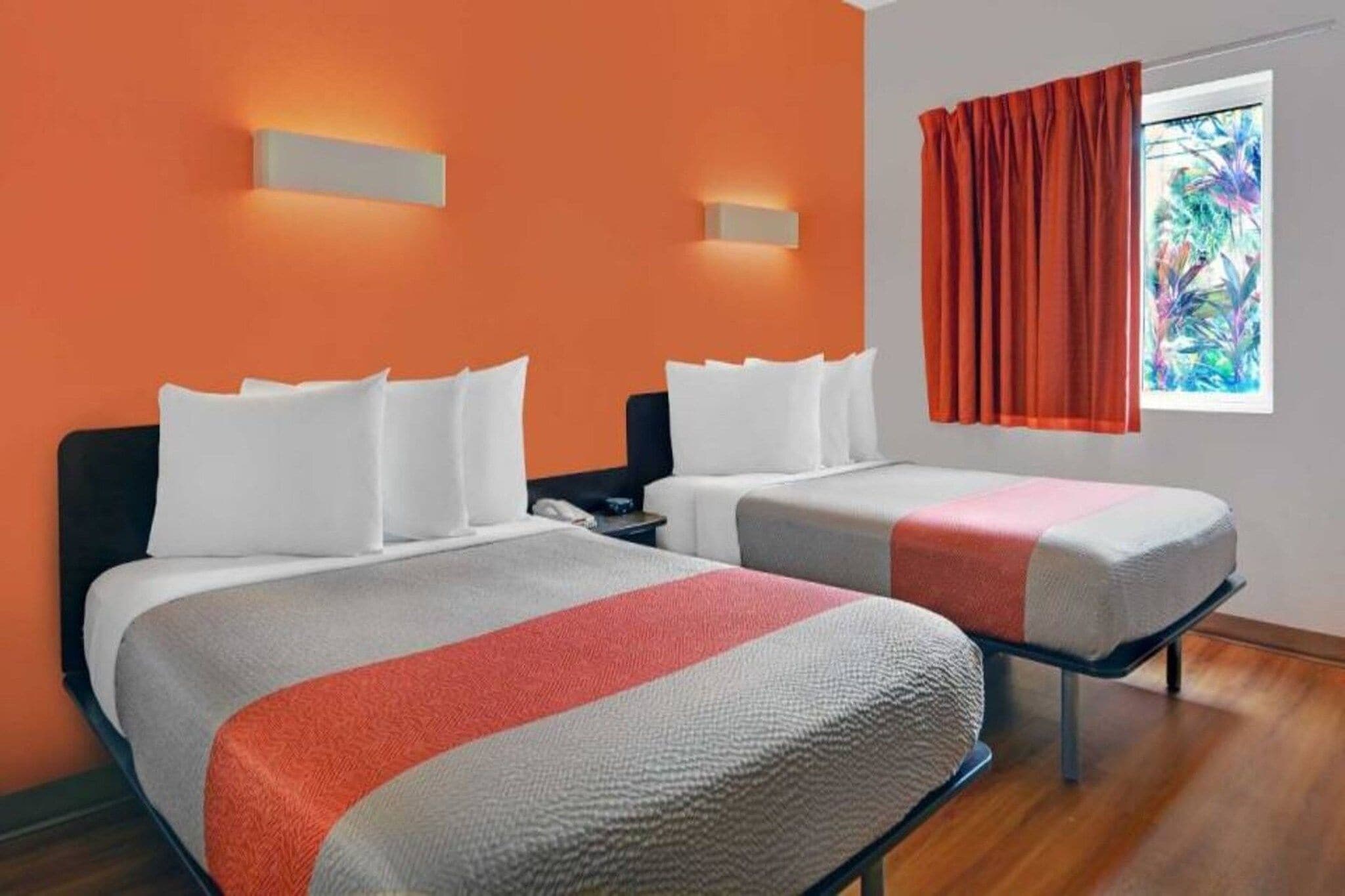 A hotel room with two beds, a nightstand, and a window with curtains.