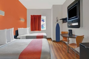 Habitació d'hotel amb dos llits, un escriptori, una cadira, un televisor i una finestra amb cortines.