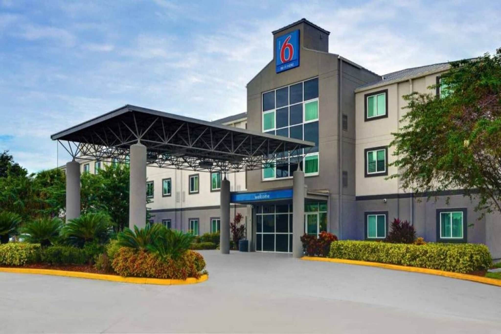 A modern hotel with a covered entrance, a prominent '6' sign, and a welcoming sign.