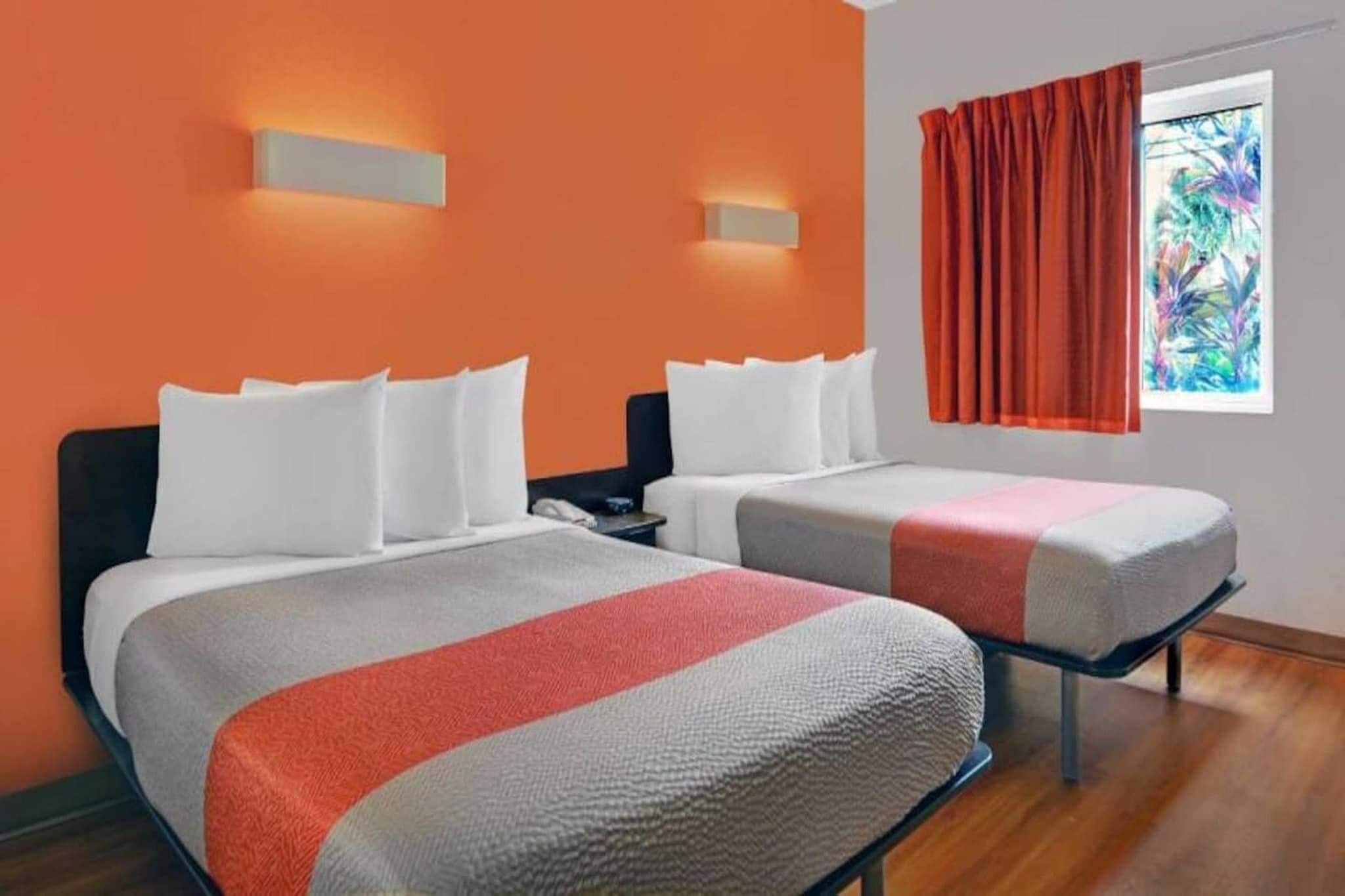 A hotel room with two beds, a nightstand, and a window with curtains.