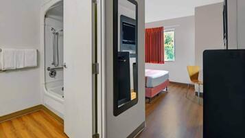 A hotel room with a shower, a bed, a chair, and a TV.