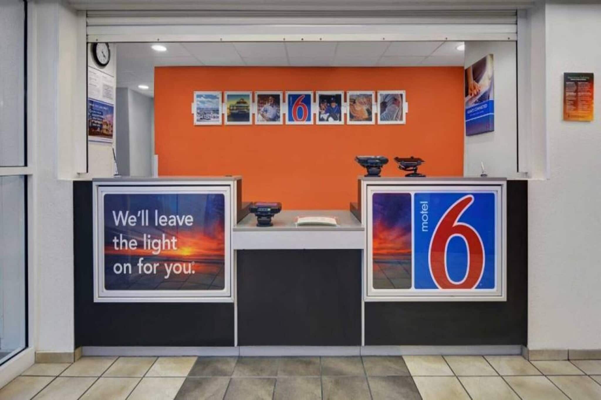 A reception desk with a clock, a sign reading 'We'll leave the light on for you.', and a 'motel 6' sign.