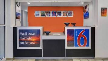 A reception desk with a clock, a sign reading 'We'll leave the light on for you.', and a 'motel 6' sign.