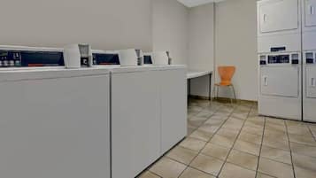 A laundry facility with multiple washing machines and dryers, a tiled floor, and a single chair.