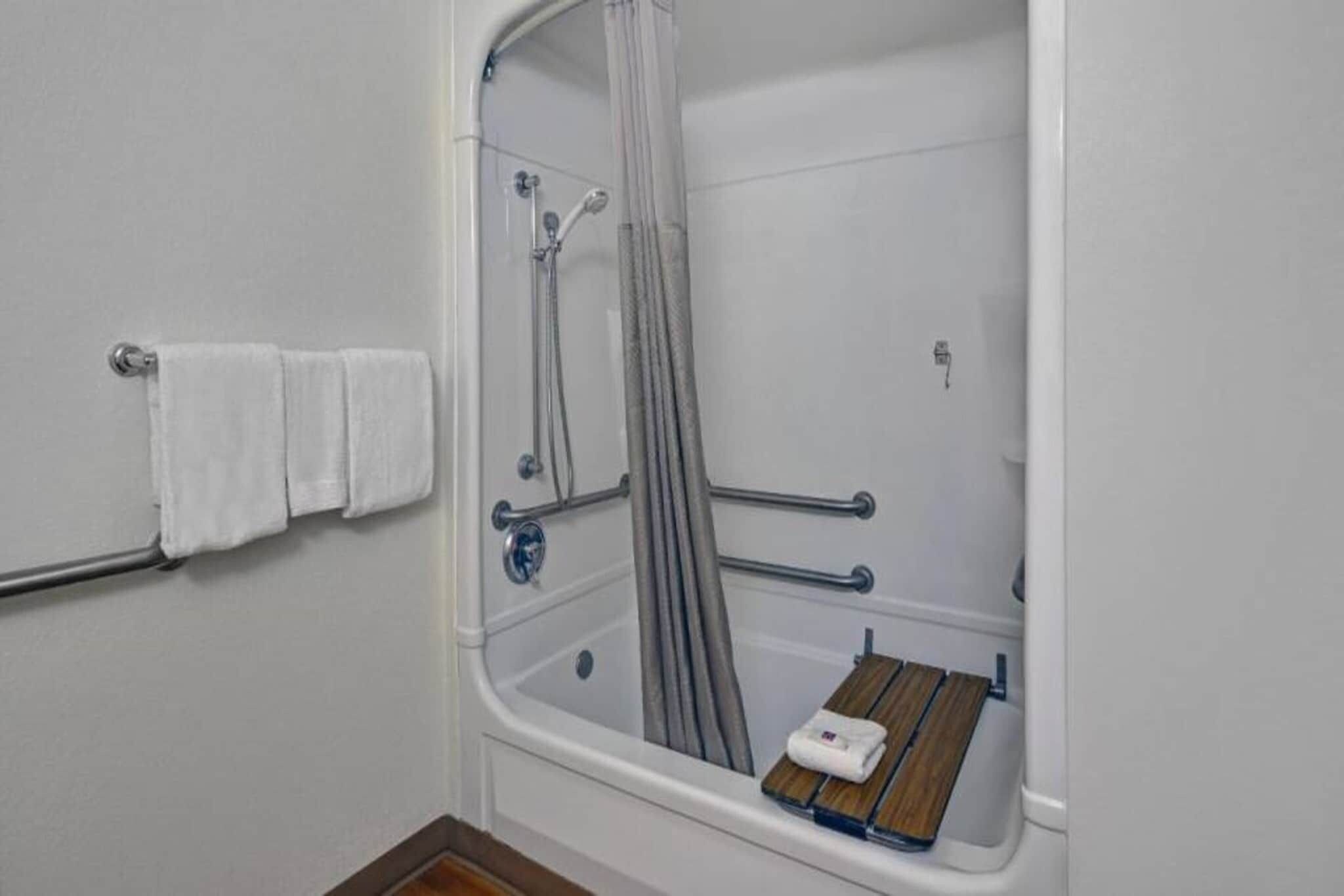 A bathroom with a shower, a bathtub, and a wooden bench.