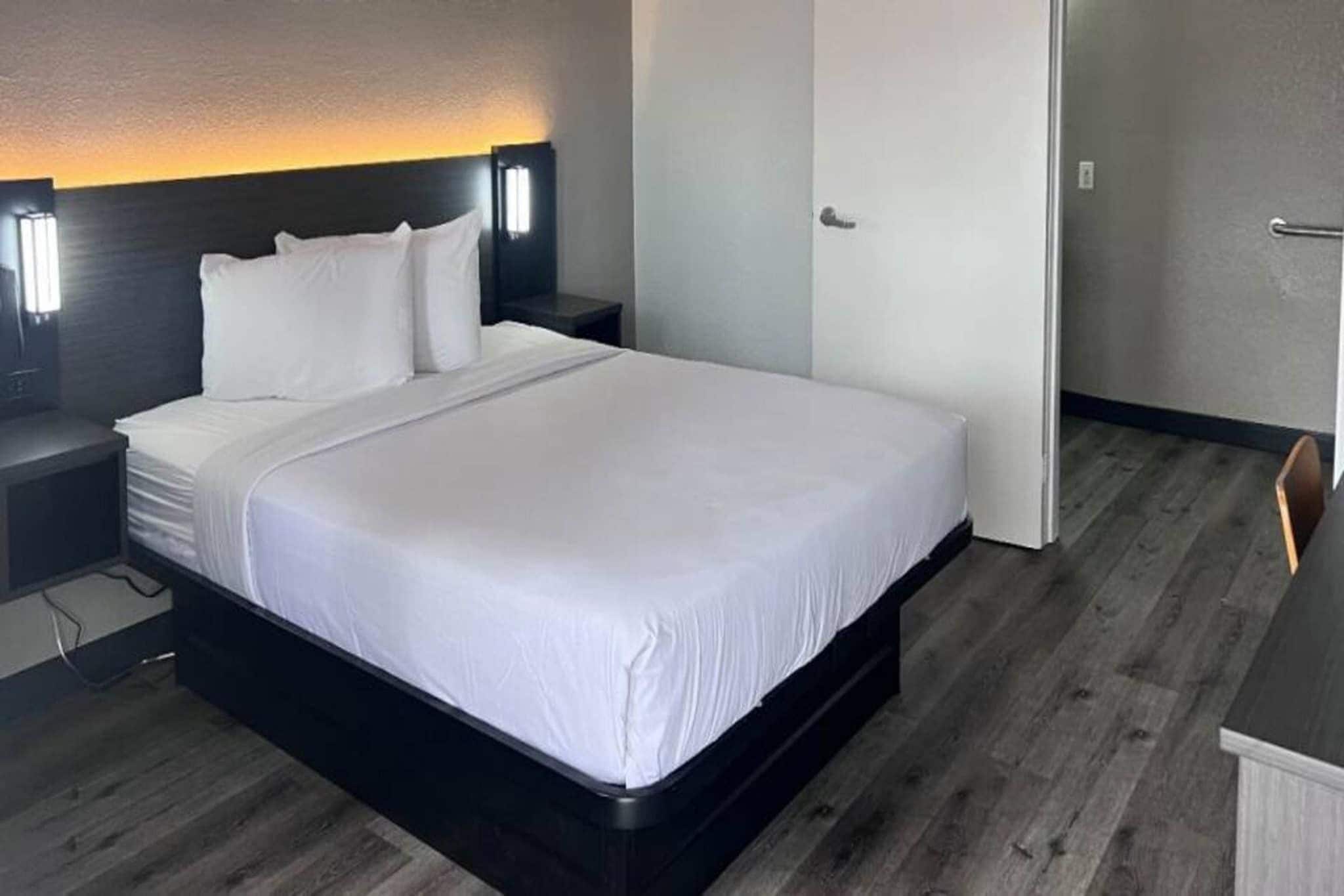Une chambre d’hôtel avec un grand lit, une table de chevet, une lampe fixée au mur et une porte.