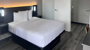 Une chambre d’hôtel avec un grand lit, une table de chevet, une lampe fixée au mur et une porte.