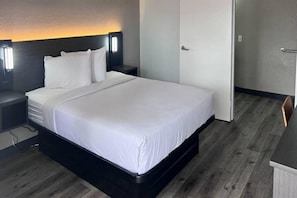 A hotel room with a large bed, a nightstand, a wall-mounted lamp, and a door. - 1 Queen Bed | Micfridge (Orlando FL)