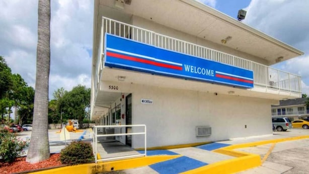 Um edifício com uma placa de 'WELCOME', varanda e área de estacionamento.