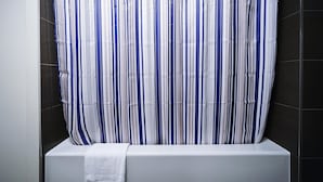 Une salle de bain avec un rideau de douche à rayures, une baignoire blanche et des murs recouverts de carreaux foncés.
