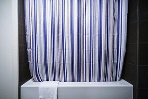 Ett badrum med ett randigt duschdraperi, ett vitt badkar och mörka kaklade väggar.