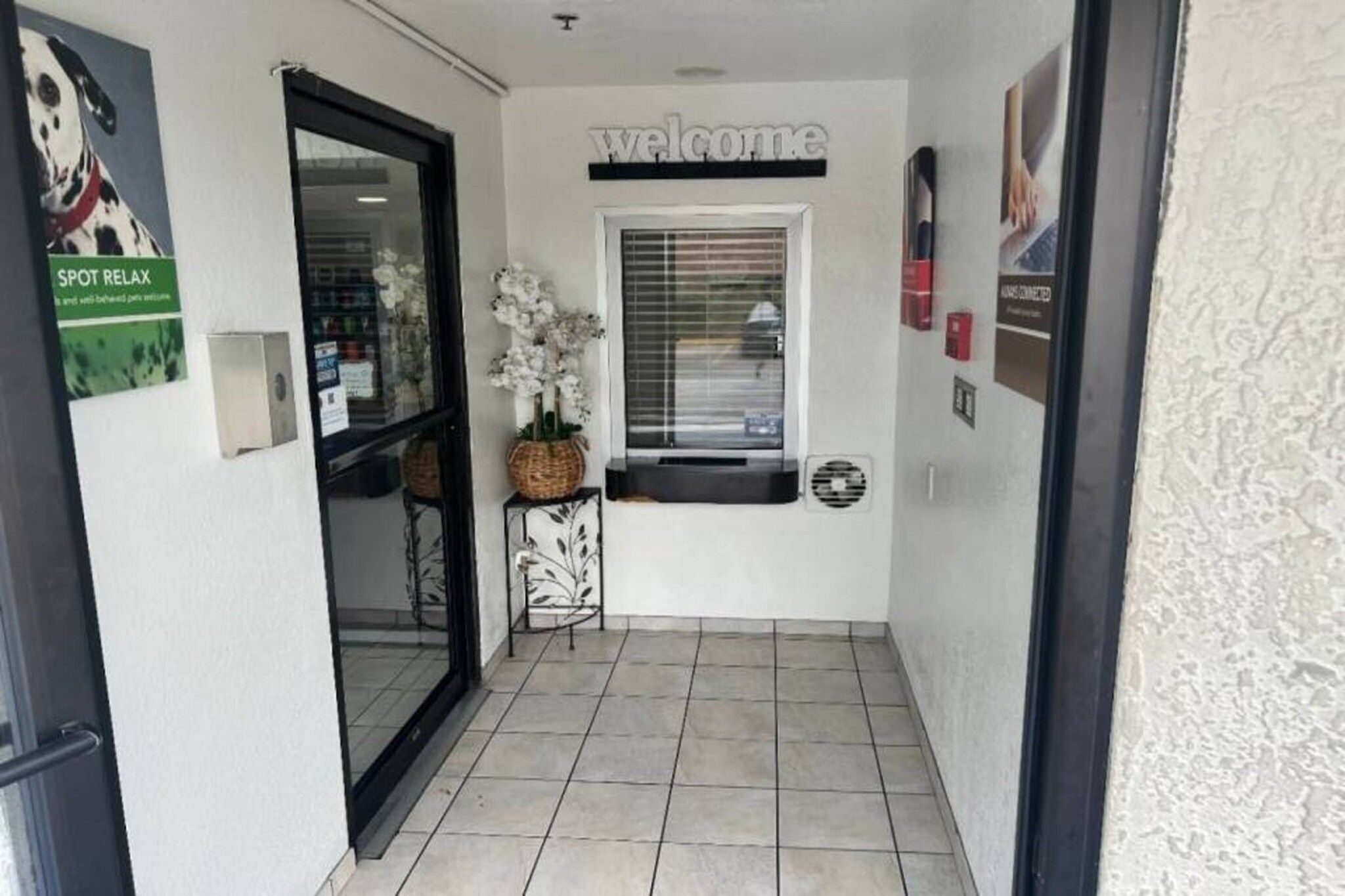 A hallway with a welcome sign, a window with blinds, a wall-mounted sign, and a door.